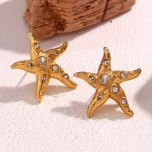 Macro detail of 18K gold starfish stud earrings with sparkling crystals on water surface