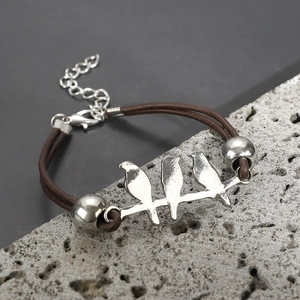 Detailed shot of bird charms on brown leather cord bracelet over a textured grey rock