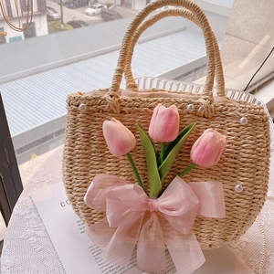 Detail of straw woven handbag featuring pink tulips, silk bow and elegant pearl accents