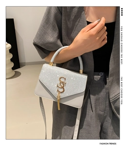Detail of silver sequined handbag featuring a golden S-logo buckle and metal fringe tassels