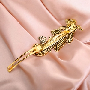 Detail of vintage gold leaf hair clip with intricate vine patterns on pink satin fabric