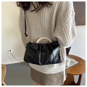 Detail of black pleated cloud bag with pearl handle worn by a model in a cozy indoor setting