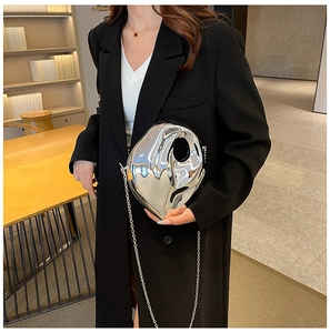 Silver metallic asymmetric clutch bag with chain strap shown on a model in a modern room