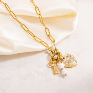 Detail of gold heart pendant with crystals, key, and pearls on a textured silk background