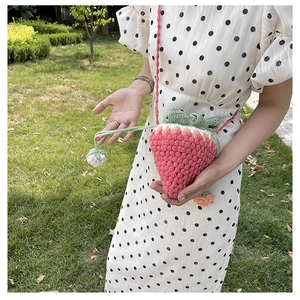Detail of pink knitted strawberry crossbody bag with green leaf top on a field
