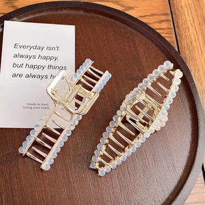 Elegant gold alloy shark hair clips with milky white beads on a rustic wooden tray