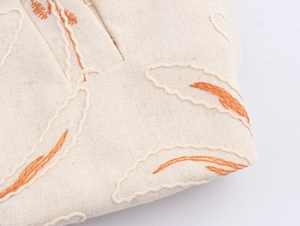 Close-up of orange floral embroidery detail on cream linen fabric bomber jacket