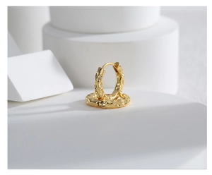 Detailed view of gold plated brass hoop earrings with hammered texture on white stone
