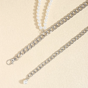 Detail of silver Cuban chain with white pearls and lobster clasp on beige texture