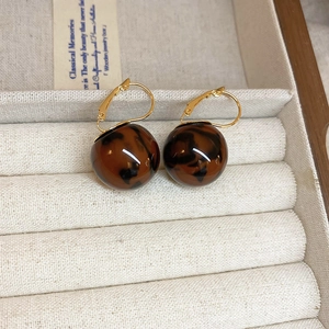Detailed close-up of retro leopard print ball earrings with gold-toned hooks on a display box