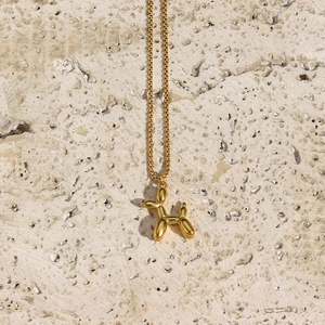Top view of a gold balloon dog pendant necklace on a beige textured stone background