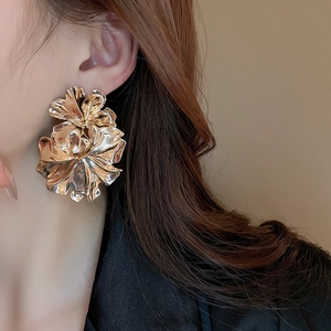 Macro side view of a large gold pleated floral earring with irregular metallic petal textures