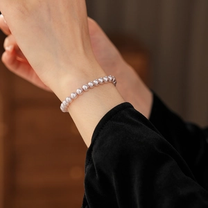Detailed view of elegant mauve pearl beaded bracelet worn on wrist with dark sleeve
