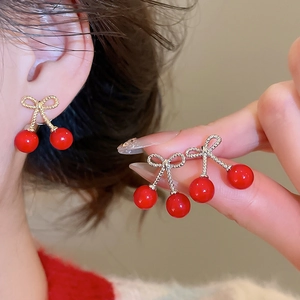 Detailed close-up of cherry stud earrings with red resin beads and golden bow detail