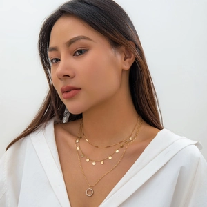 Close-up of triple-layered gold necklace with sequins and a crystal-encrusted circle pendant