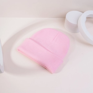 Gros plan d'un bonnet en maille rose avec texture fine et revers sur des supports blancs