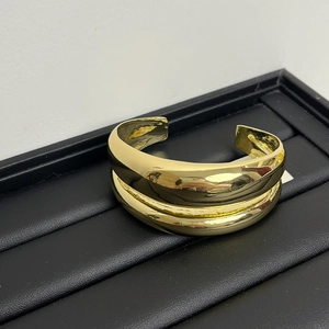Close-up of golden double-layered minimalist open cuff bracelet with irregular glossy finish