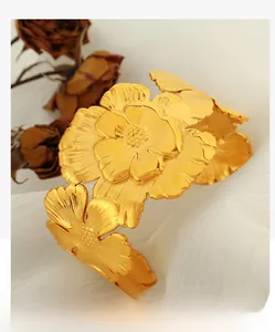 Detailed close-up of golden camellia floral cuff bracelet on white silk fabric background