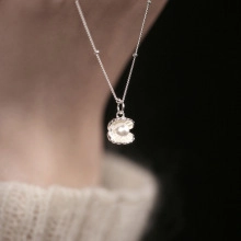 Close-up of a silver shell pendant necklace with a pearl detail on a model neck