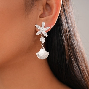 Close-up of ocean-themed silver starfish and shell earrings worn by a female model