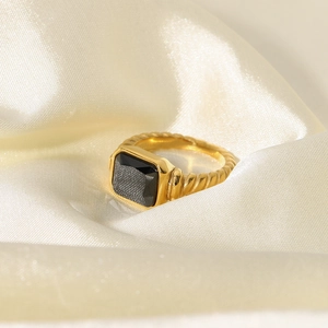 Macro detail of a gold twisted ring featuring a large rectangular black gemstone on silk