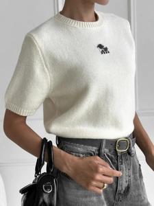 Dettaglio di un top in maglia bianca a maniche corte con ricamo di cane nero sul petto