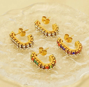Macro shot of U-shaped gold earrings with white and colorful zircon crystals on a glass plate