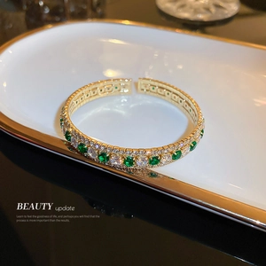 Elegant gold open bangle with sparkling cubic zirconia and emerald green stones