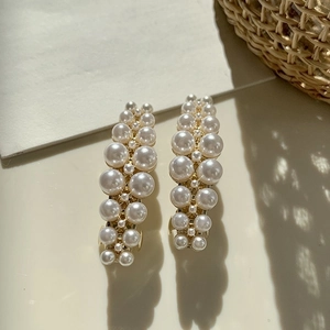 Elegant gold metal hair clips set with glossy white pearls in a warm sunlight setting