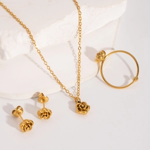 Close-up of golden rose pendant necklace ring and earrings set on white stone decor