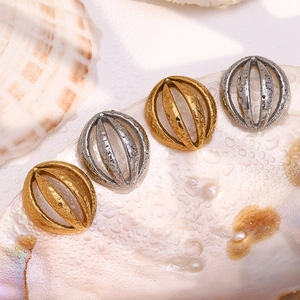 Macro detail of gold and silver hollow sphere stud earrings on white shell background