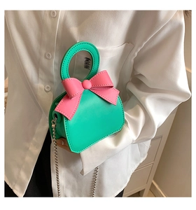 Close-up of green PU leather mini bag with pink bow and silver metal chain strap