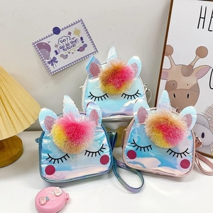 Three holographic unicorn shoulder bags with colorful plush pom-poms on a white desk