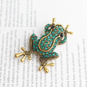 Dettaglio macro della spilla a rana con strass verdi su montatura in lega d'oro vintage