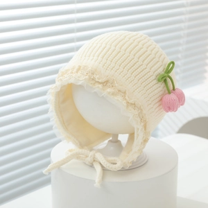 Detail of baby knit hat with cream lace trim, pink cherry accents and ear flaps
