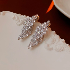 Macro shot of silver zircon leaf earrings on white carved plaque with dark red background