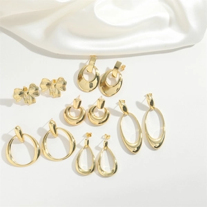 Flat lay of diverse gold hollow earrings with bow and hoop designs on white satin