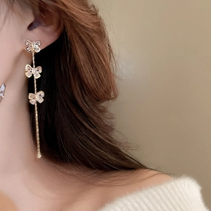 Détail de boucles d'oreilles nœuds dorées avec cristaux portées par un modèle