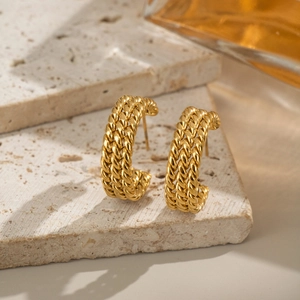 Detail of gold triple-layered twisted hoop earrings on a textured stone base