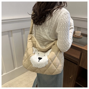 Detail of a large beige quilted tote bag with a plush dog patch on a model's shoulder