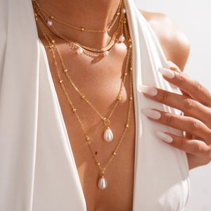 Close-up of layered gold necklace with teardrop pearl pendants on a fashion model