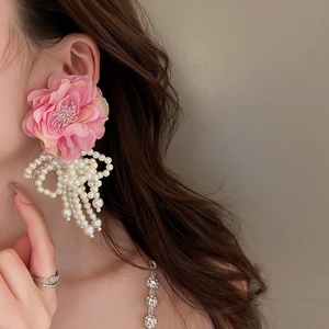 Close-up of pink flower earring with long white pearl tassels worn by a model