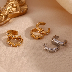 Macro shot of 18K gold and silver C-shaped ear cuffs with sparkling zircons on silk