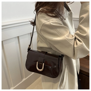 Detail of dark brown patent leather shoulder bag with golden horseshoe buckle on a model