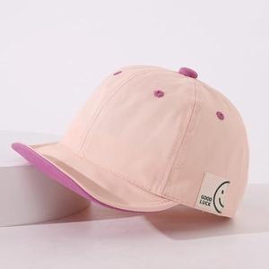 Detailed view of pink baby baseball cap featuring soft brim and Good Luck smile patch