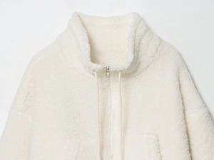 Close-up of cream white sherpa fleece jacket featuring stand-up collar and silver zipper