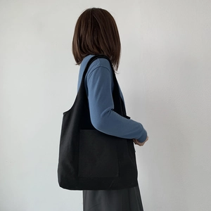 Black canvas tote bag with front pocket shown on a model for daily use and travel