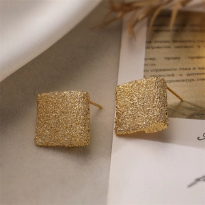 Macro detail of golden teardrop earrings with a textured sandblasted matte finish