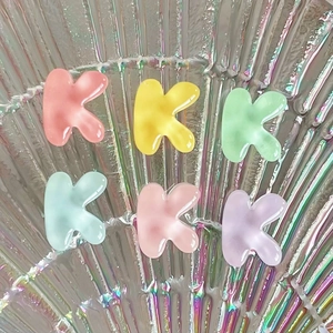 Close-up of small K-shaped translucent resin charms in colorful pastel gradient hues