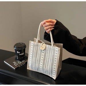 Detail of linen tote bag featuring black vertical stripes and a large decorative wooden button